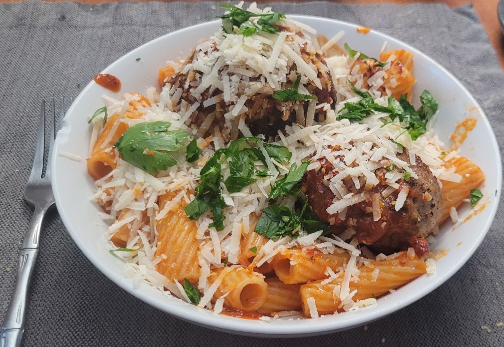 A plate of rigatoni and meatballs, covered in an unreasonable amount of Parmesan cheese.